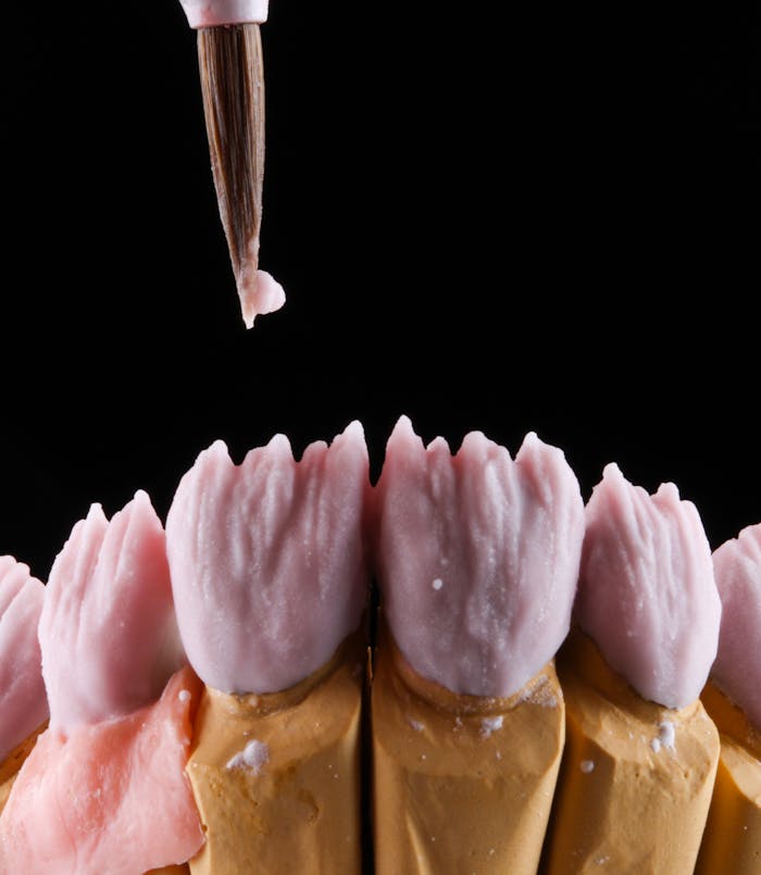 Close-up of a dental mold being crafted with artistic precision using a brush on a black background.